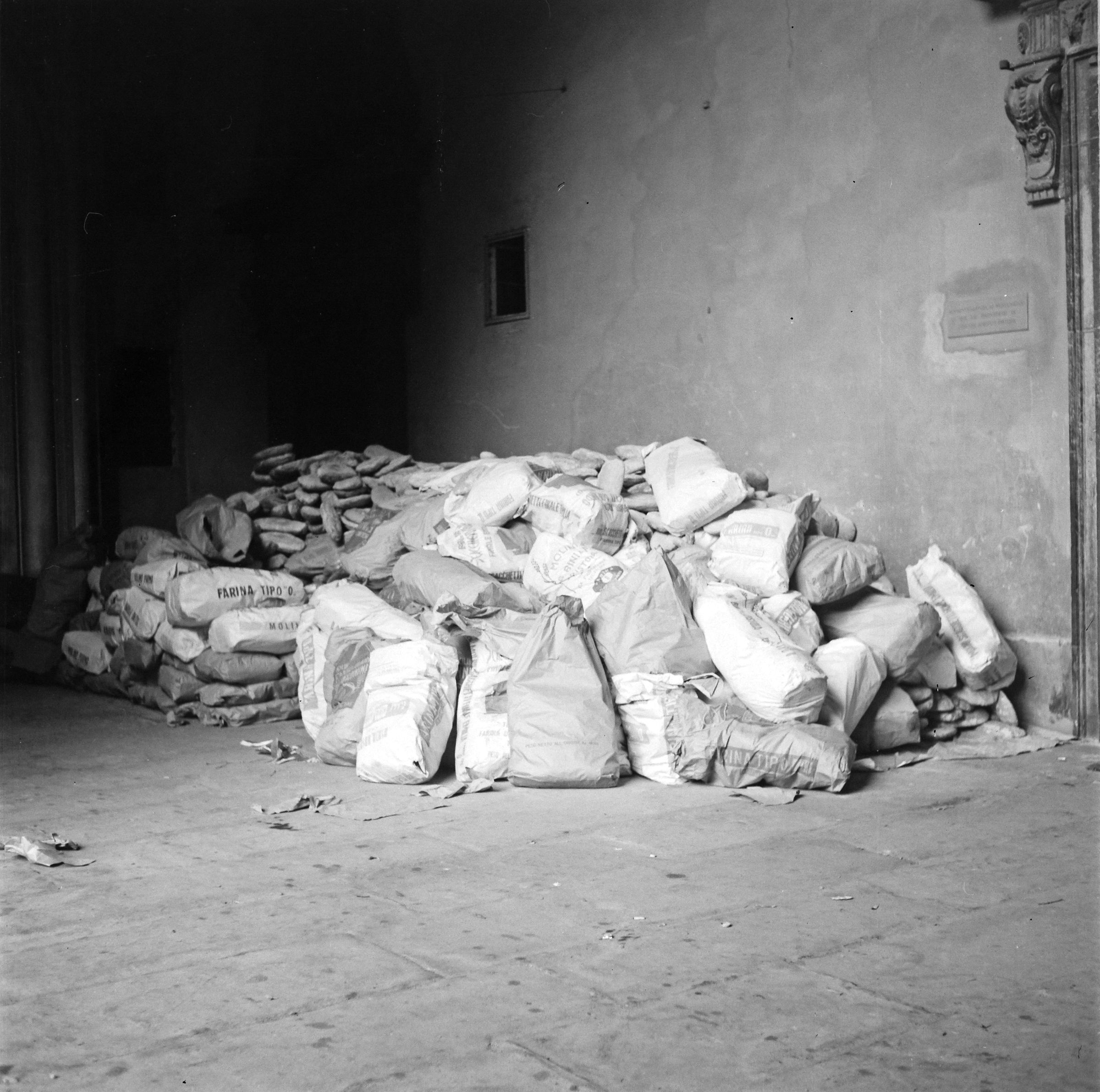 Fotografo non identificato, Firenze - Palazzo Pitti, sacchi accatastati di pane per gli alluvionati nel cortile del palazzo, 1966, gelatina ai sali d'argento, 6x6cm, N003770
